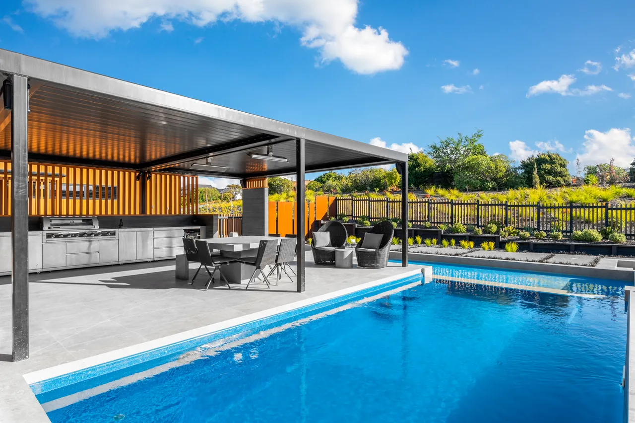 Pool beside a covered patio with outdoor kitchen, dining area and lounge chairs